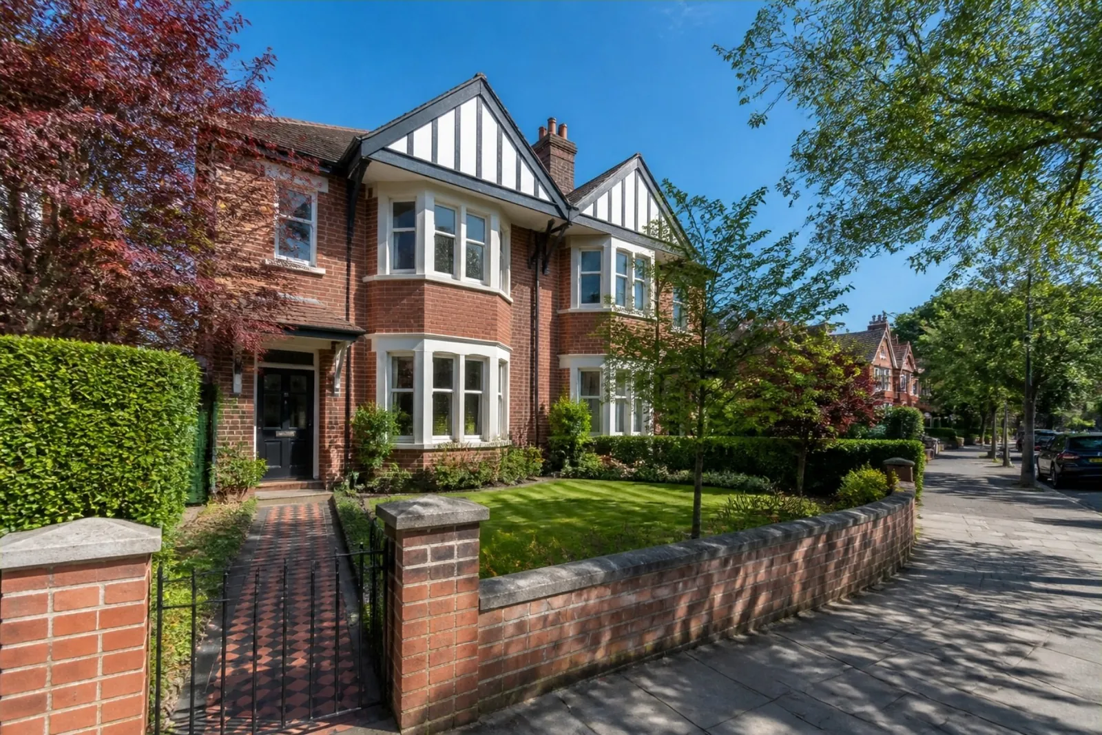 Edwardian red-brick semi with a neat striped front lawn, low brick wall and tiled path on a leafy street