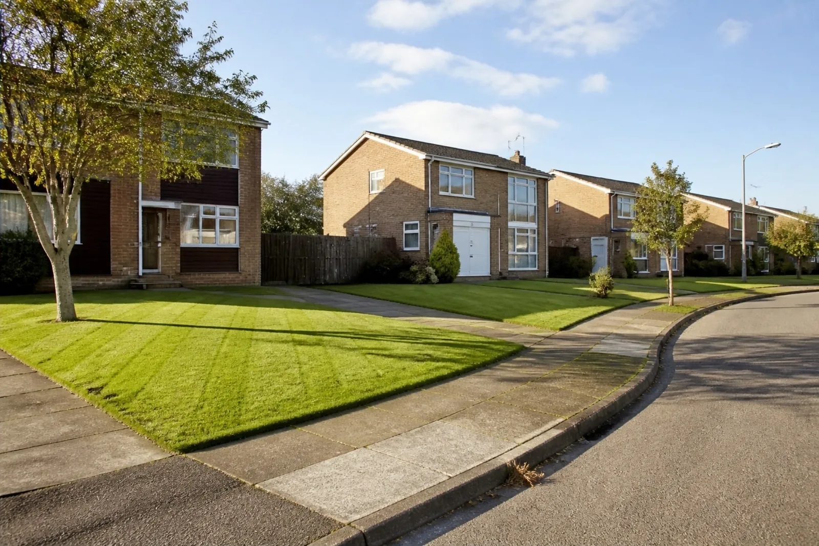 Cul-de-sac of 1970s brick homes with open-plan front lawns, one freshly returfed and bright green